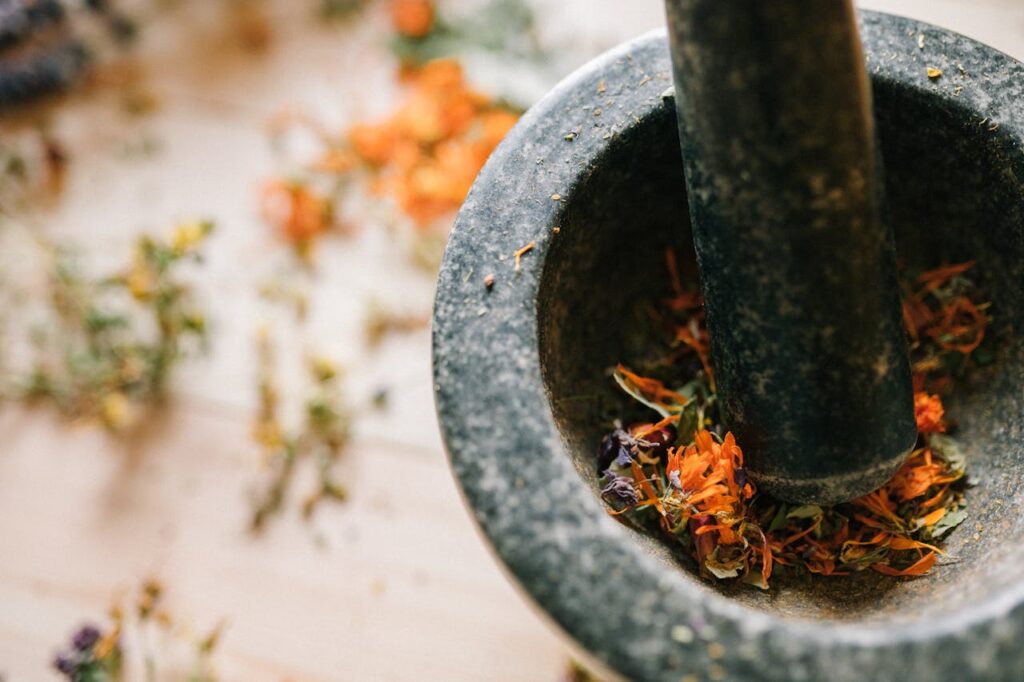 Close-up of a stone mortar and pestle grinding vibrant dried flowers on a wooden surface.